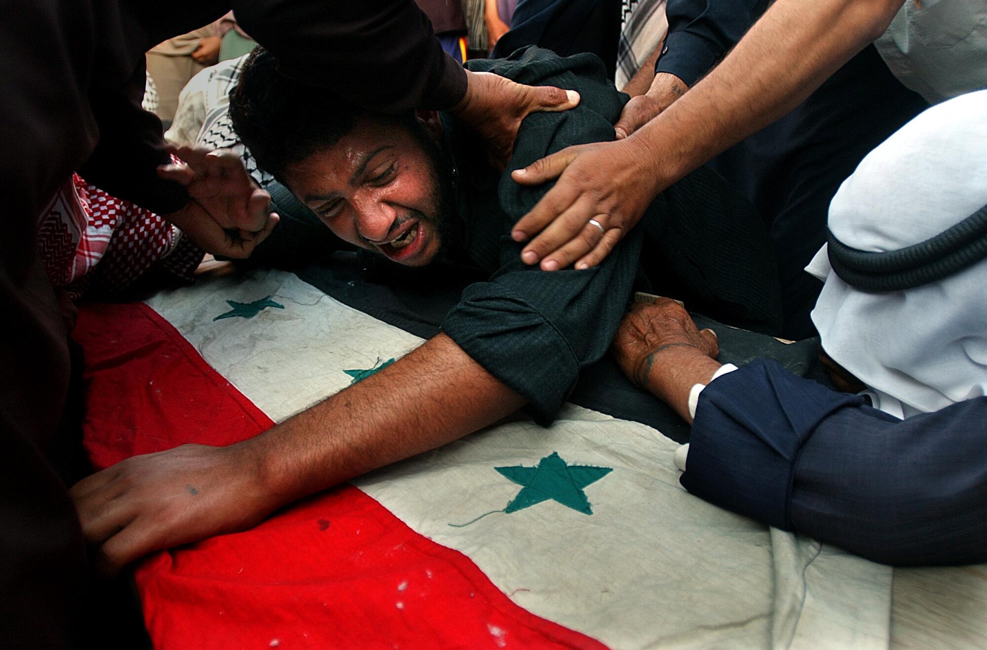 Hamed Hamid Hussein clutches his brother's casket as he screams out "Is this what he deserves?"