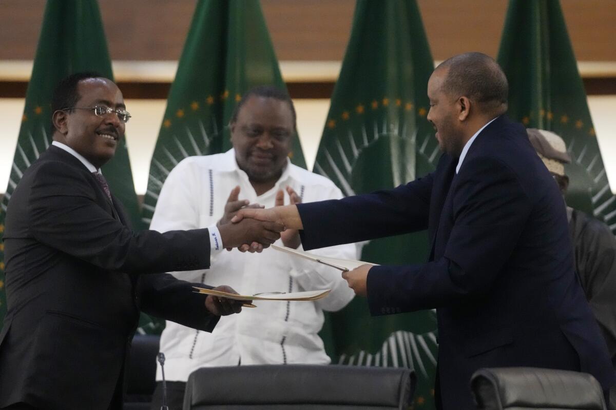 Two men shake hands as a third man applauds.