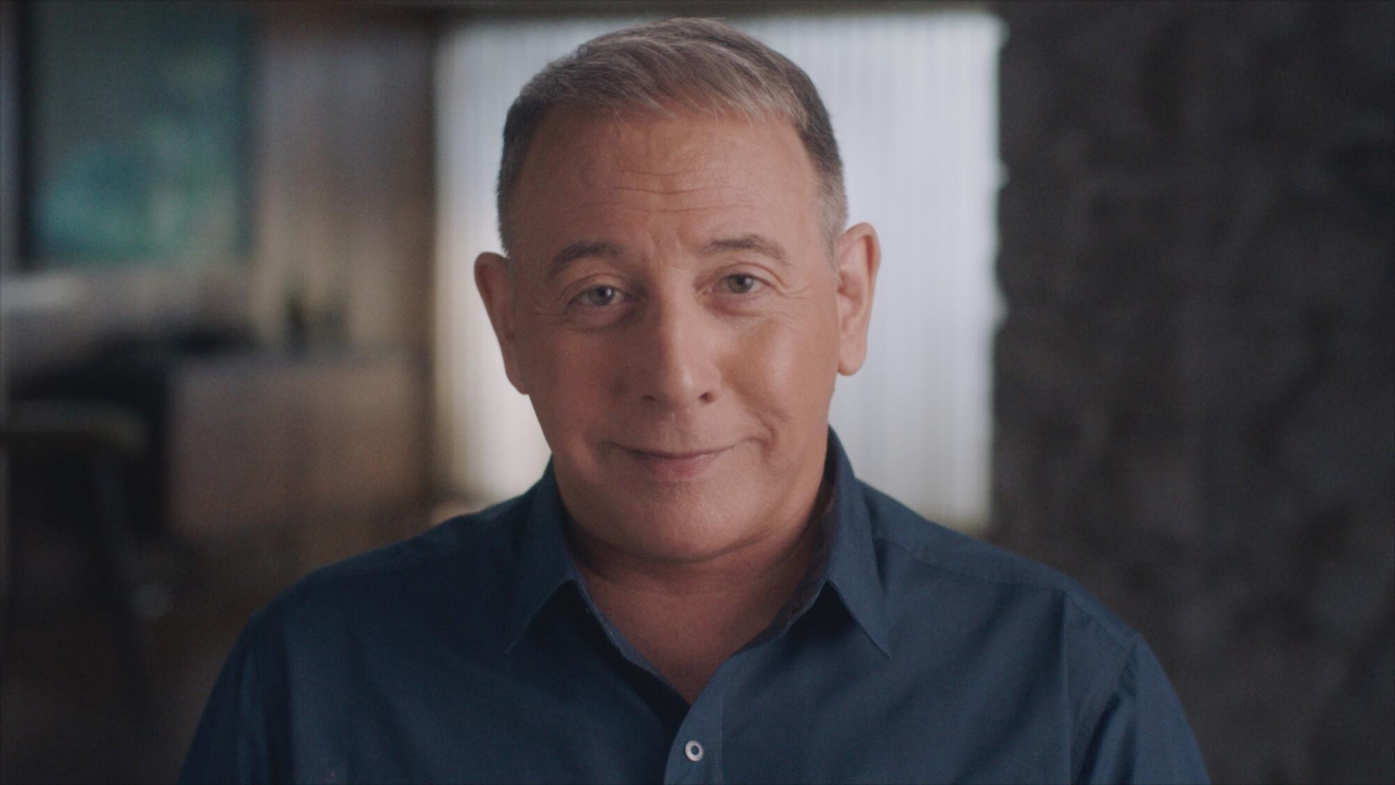 A grey haired man in a blue shirt sitting.