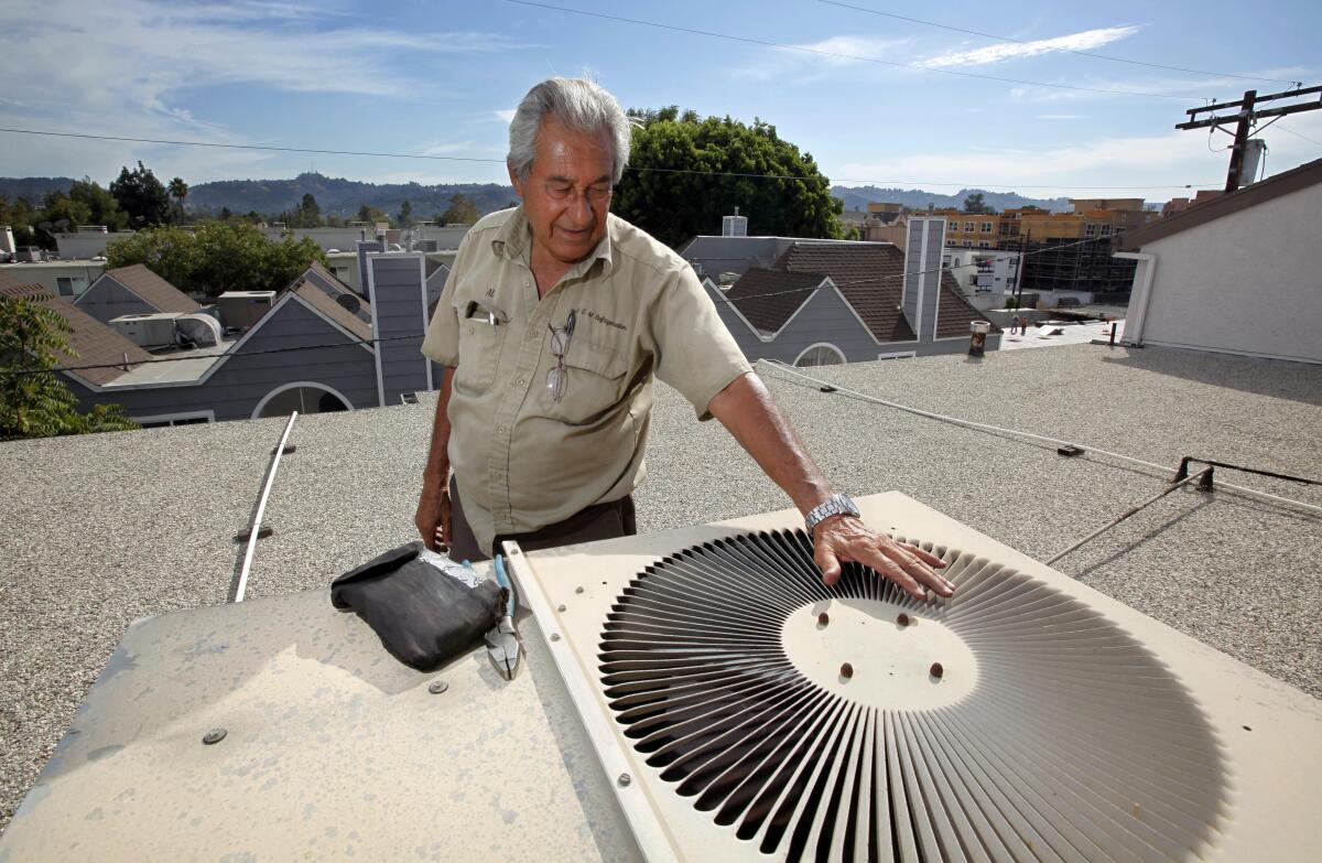 A man stands on a flat rooftop and hovers his open palm over a circular opening of an air conditioning vent.