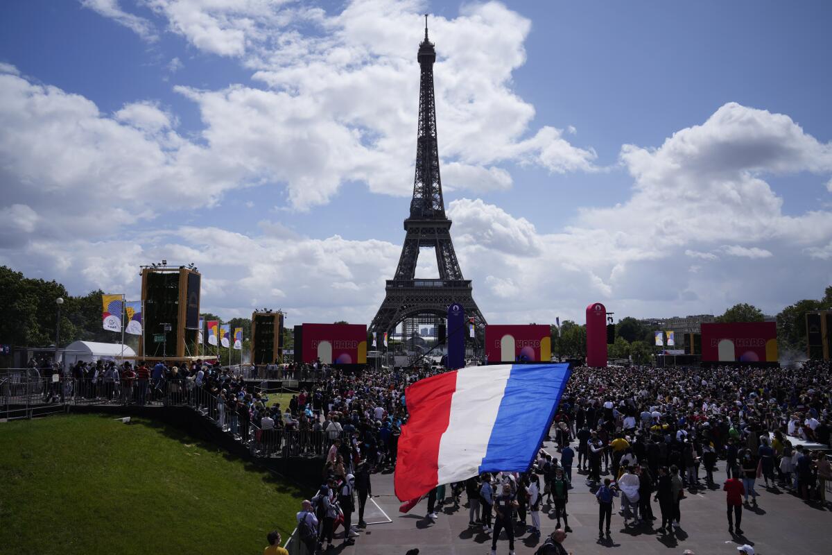 A man unfurls a French flag at the Olympics fan zone at Trocadero Gardens in front of the Eiffel Tower in Paris, Sunday, Aug. 8, 2021. A giant flag will be unfurled on the Eiffel Tower in Paris Sunday as part of the handover ceremony of Tokyo 2020 to Paris 2024, as Paris will be the next Summer Games host in 2024. The passing of the hosting baton will be split between the Olympic Stadium in Tokyo and a public party and concert in Paris. (AP Photo/Francois Mori)