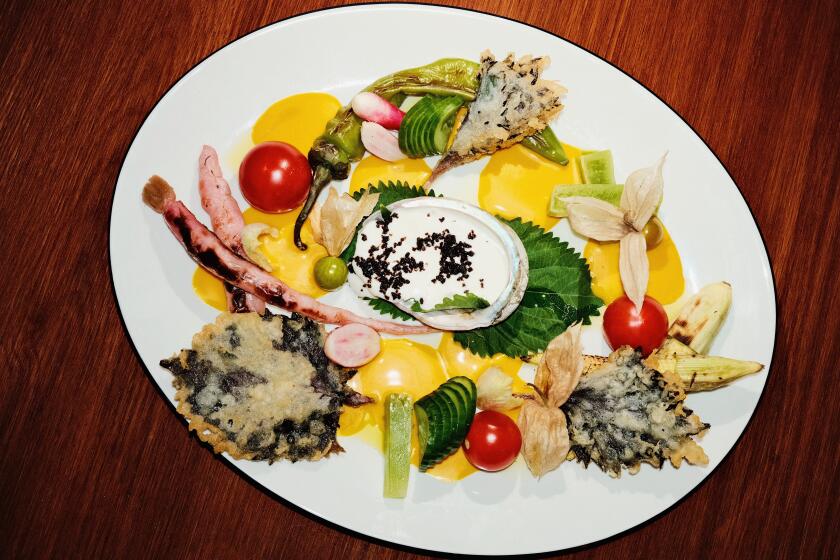 An overhead of a crudités plate featuring fried shiso leaves, pickled carrots, raw cucumber and tomatoes and ground cherries