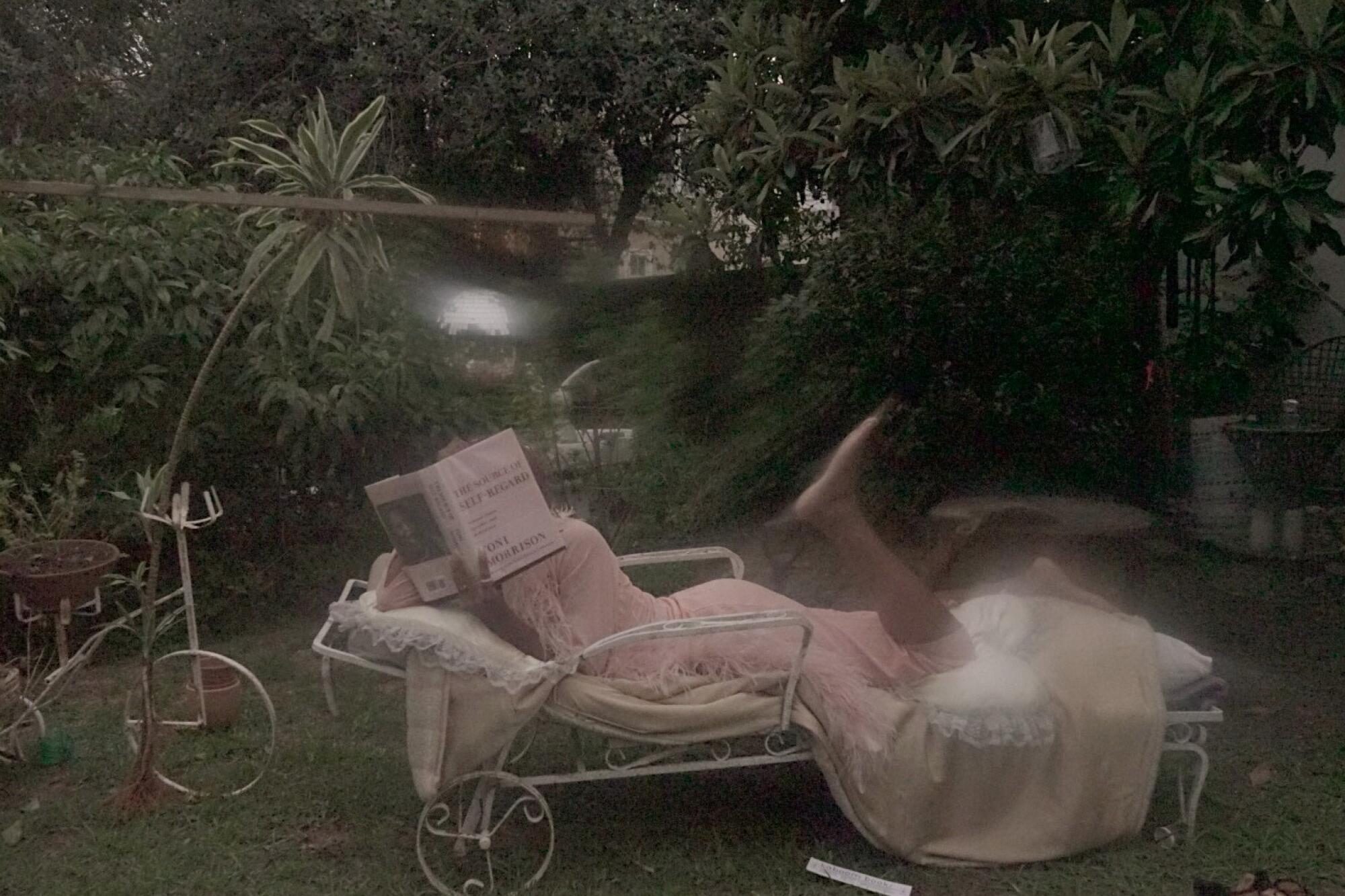 A woman leans on a chaise longue outside, reading Toni Morrison's “The Source of Self-Regard."