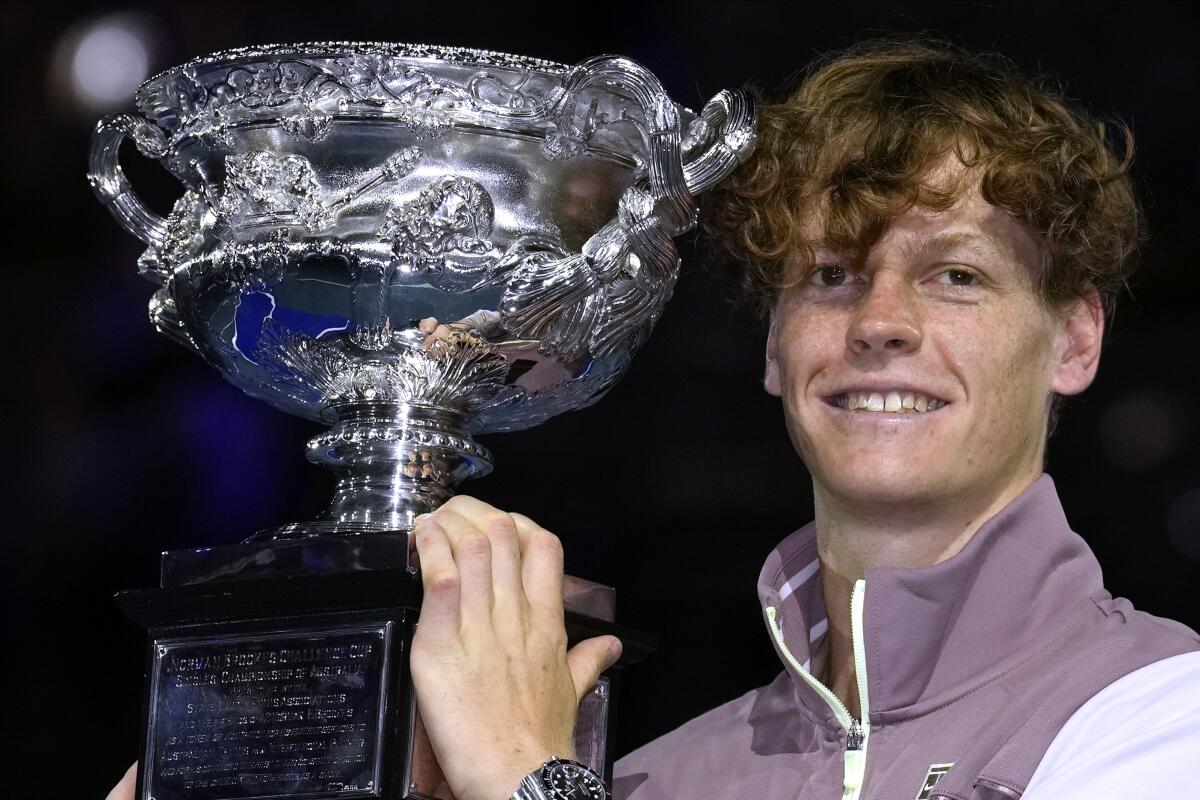 Jannik Sinner smiles and holds up a trophy after defeating Daniil Medvedev to win the Australian Open