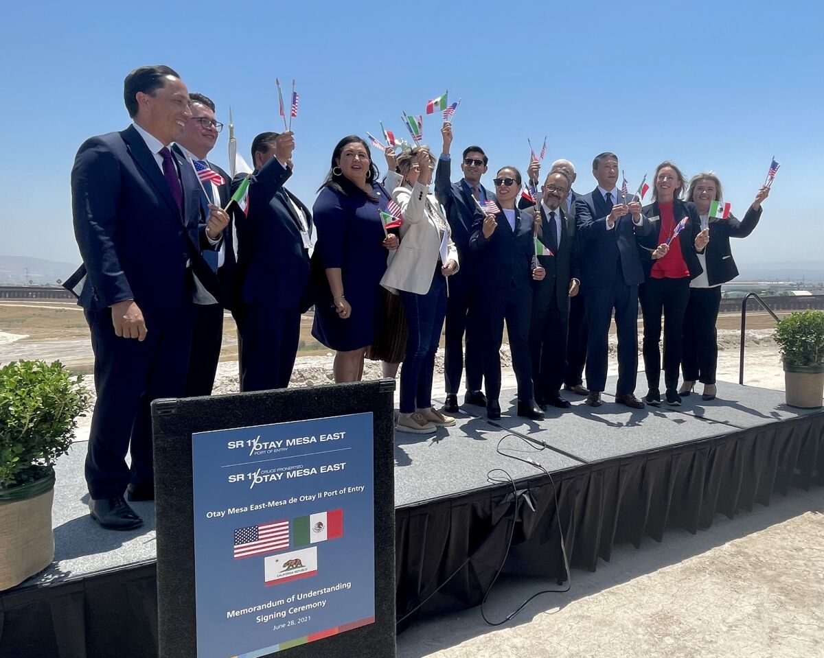Officials stand on a stage waving small Mexican and U.S. flags.