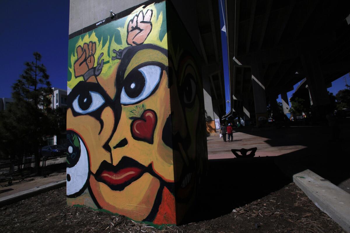 Barrio Logan residents walk past freeway columns covered with murals through Chicano Park under the ramp to the Coronado-Bay bridge.