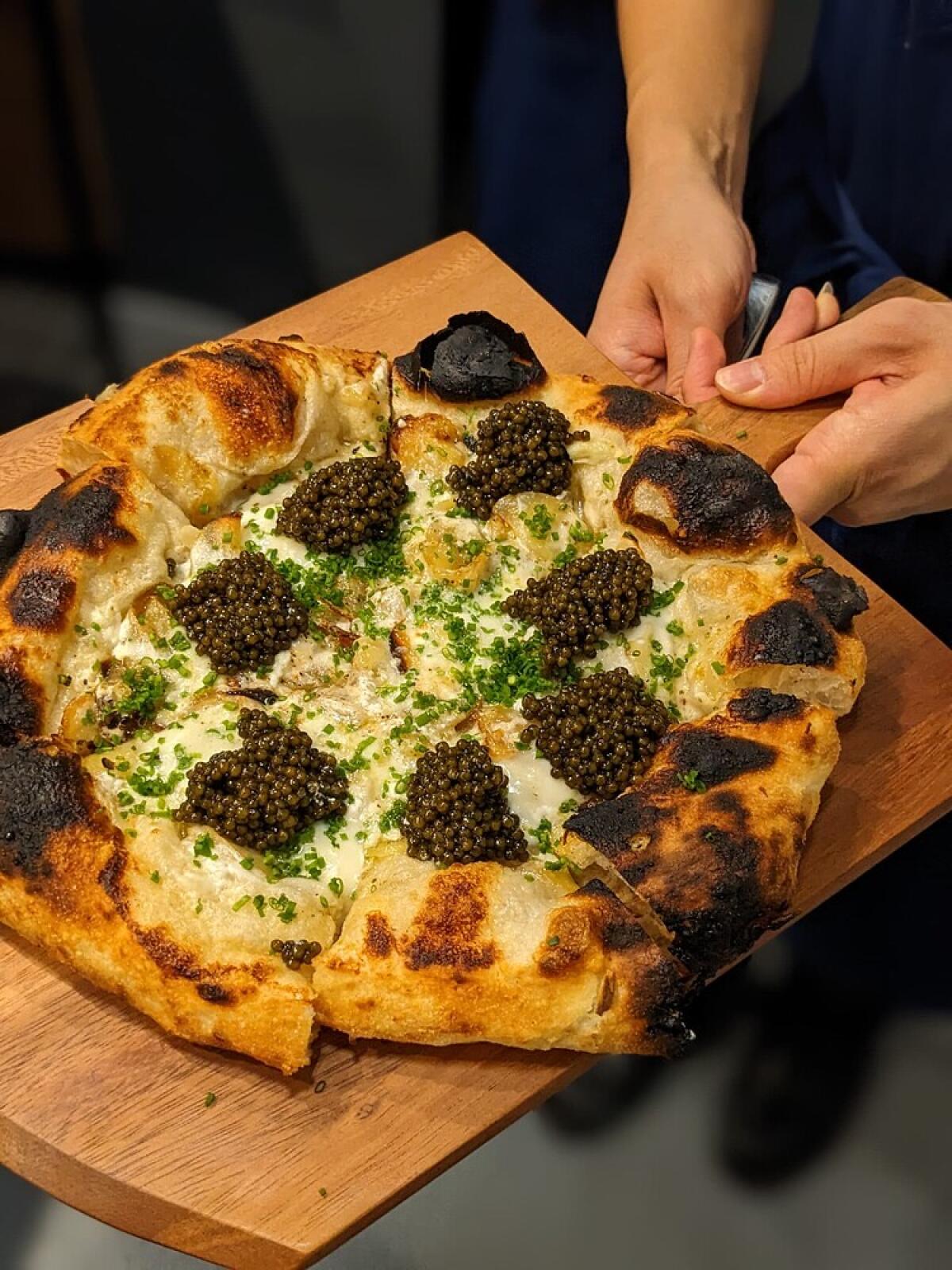 A hand holds a whole pizza, each slice topped with a mound of caviar at Pizzeria Sei's pizza omakase in Pico-Robertson.
