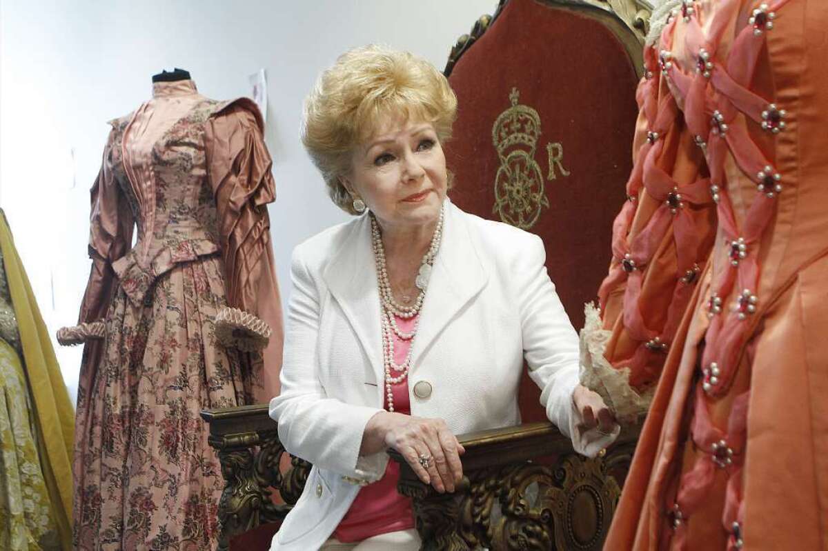 Debbie Reynolds sits on the throne from the 1955 movie "Virgin Queen" surrounded by dresses worn by Bette Davis, right, and Joan Collins in the movie. At the time of this 2011 photo, Reynolds was auctioning her massive collection of movie memorabilia.