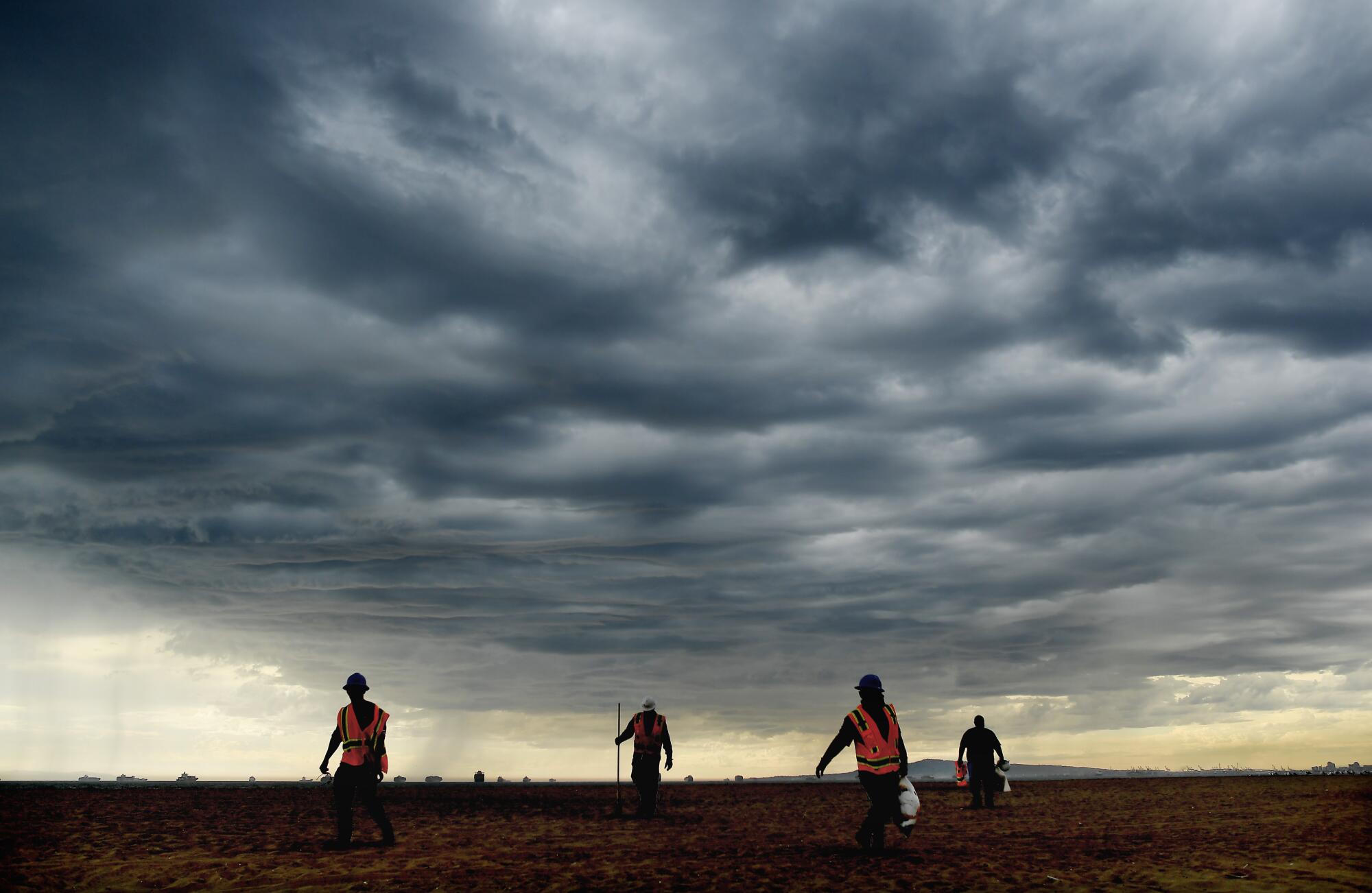 Workers in orange vests walk under dramatic dark clouds