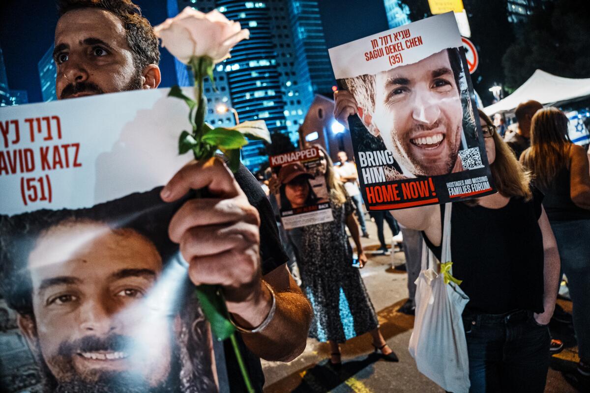 Demonstrators in a city at night hold posters of loved ones with messages including "Kidnapped" and "Bring him home now!"