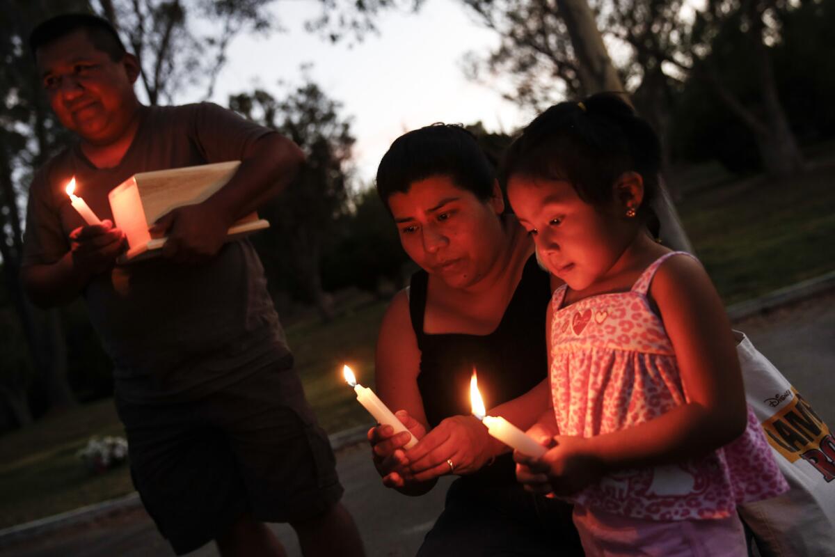 Nayo Mateo, left, holds the cremated remains of his family's dog, Maru, as his wife, Marce, and their daughter Lucie, 2, join him at a candlelight memorial service at Los Angeles Pet Memorial Park. Their Labrador retriever died in Mateo's van after it had been stolen and abandoned with the dog in it.