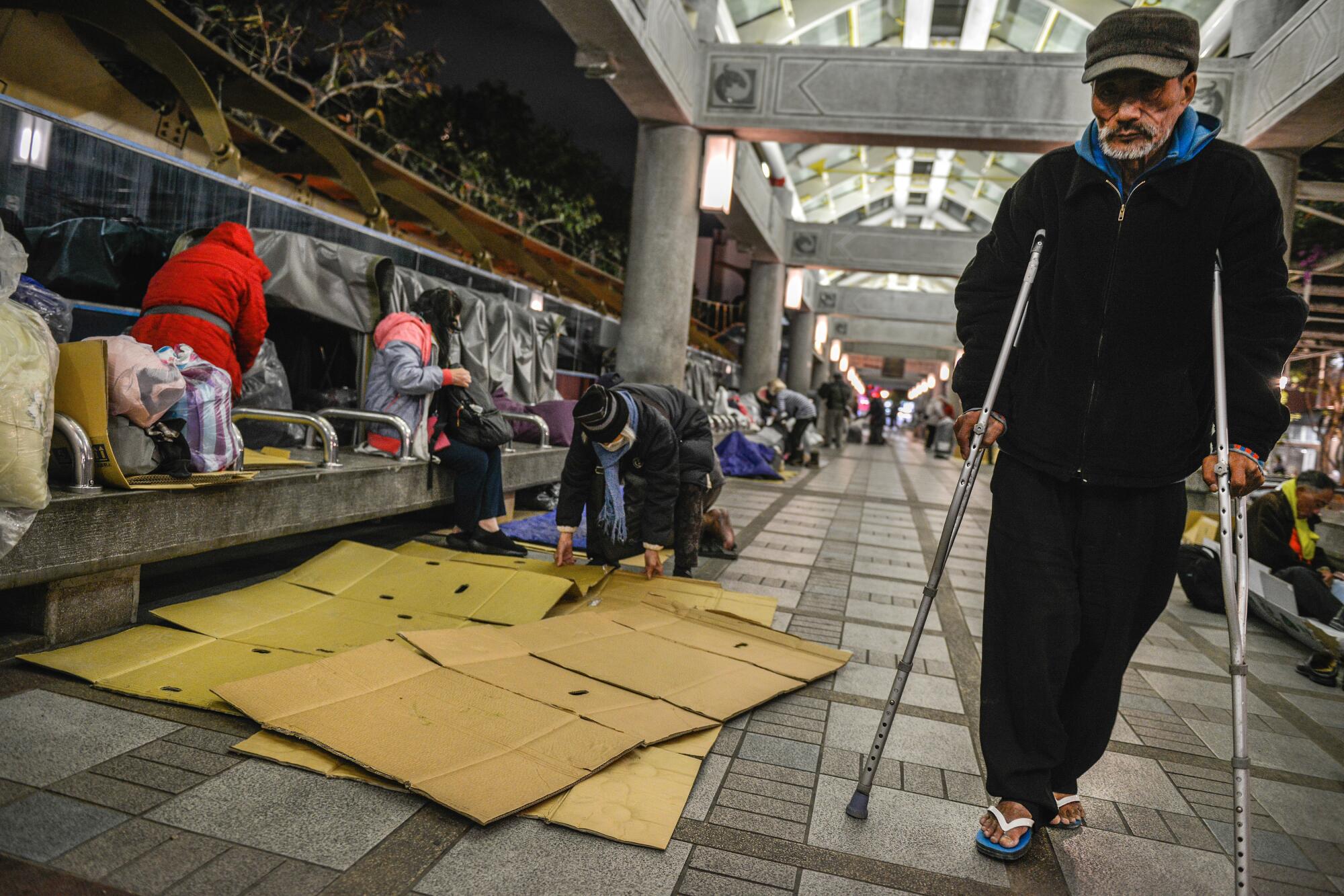 A man on crutches makes his way past other homeless people in Bangka Park in Taipei, Taiwan.