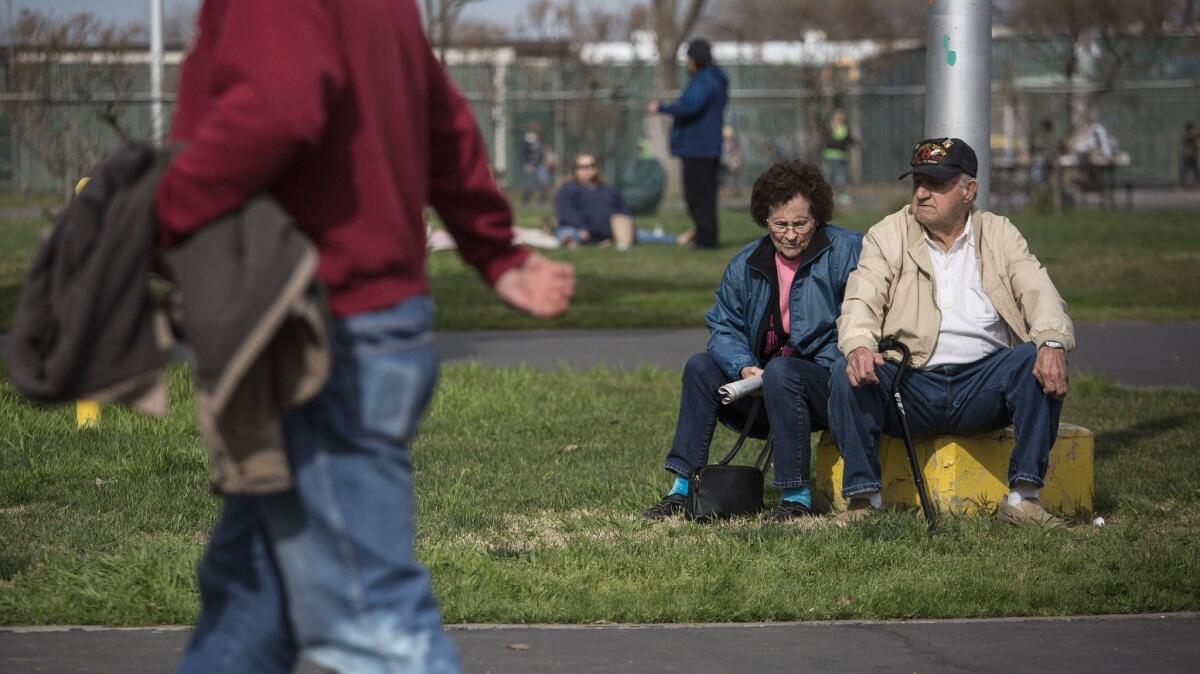 Bill O'Kelley, 86, and his wife Doris O'Kelley, 84, of Oroville sit near a flagpole at Silver Dollar Fairgrounds evacuation center in Chico, Calif.