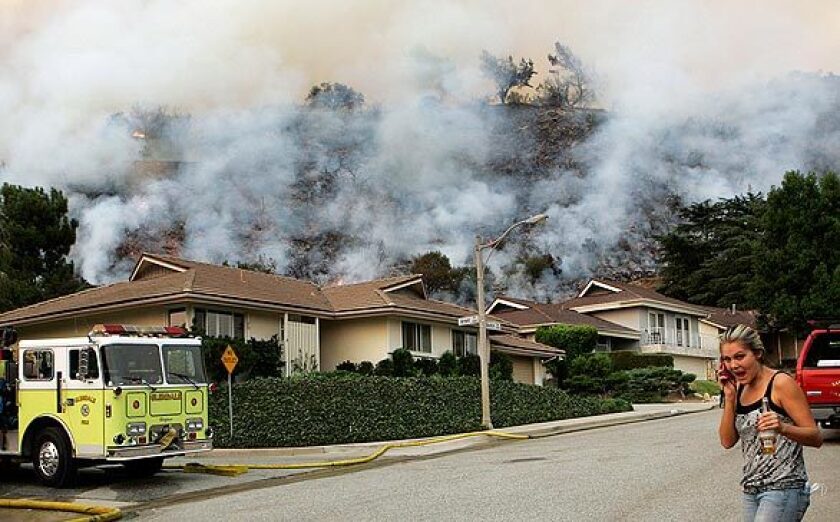 A resident talks on her cellphone as a smoky hillside looms behind homes on Boston Avenue in La Crescenta on Tuesday.