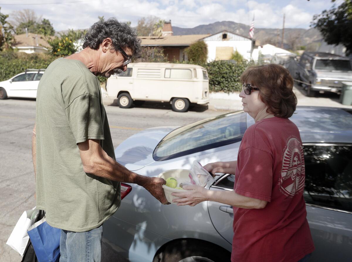 Monica Ciafardini, who sees George Contreras daily on her dog walk by Walt Disney Elementary School where Contreras is a crossing guard, gives him some dog supplies for his surviving dog Scout. His other dog, Blackie, died on Feb. 13 in a fire that tore through his home.