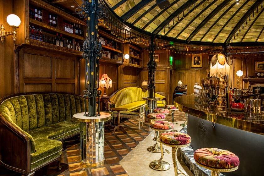 Raised by Wolves' seating area with green couches on the wall and pink padded stools at the bar.