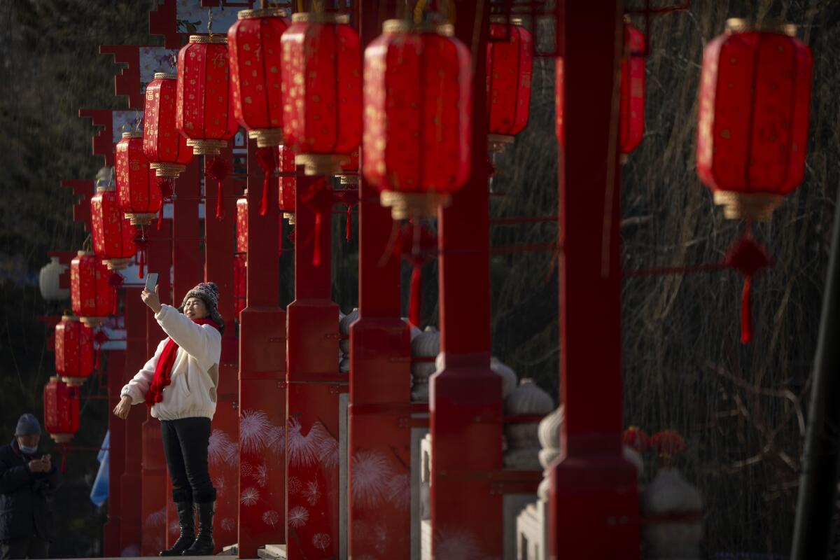 Una mujer posa para una foto en un puente decorado con faroles en un parque público de Beijing,