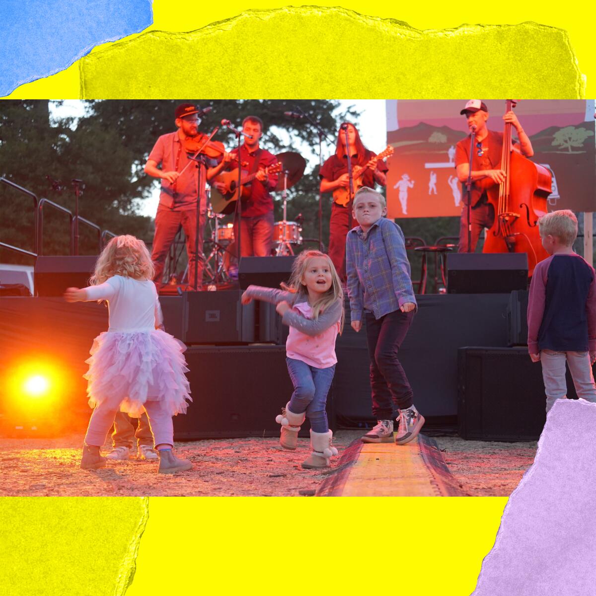 Four small children dance in front of an outdoor stage where a four-piece band plays.