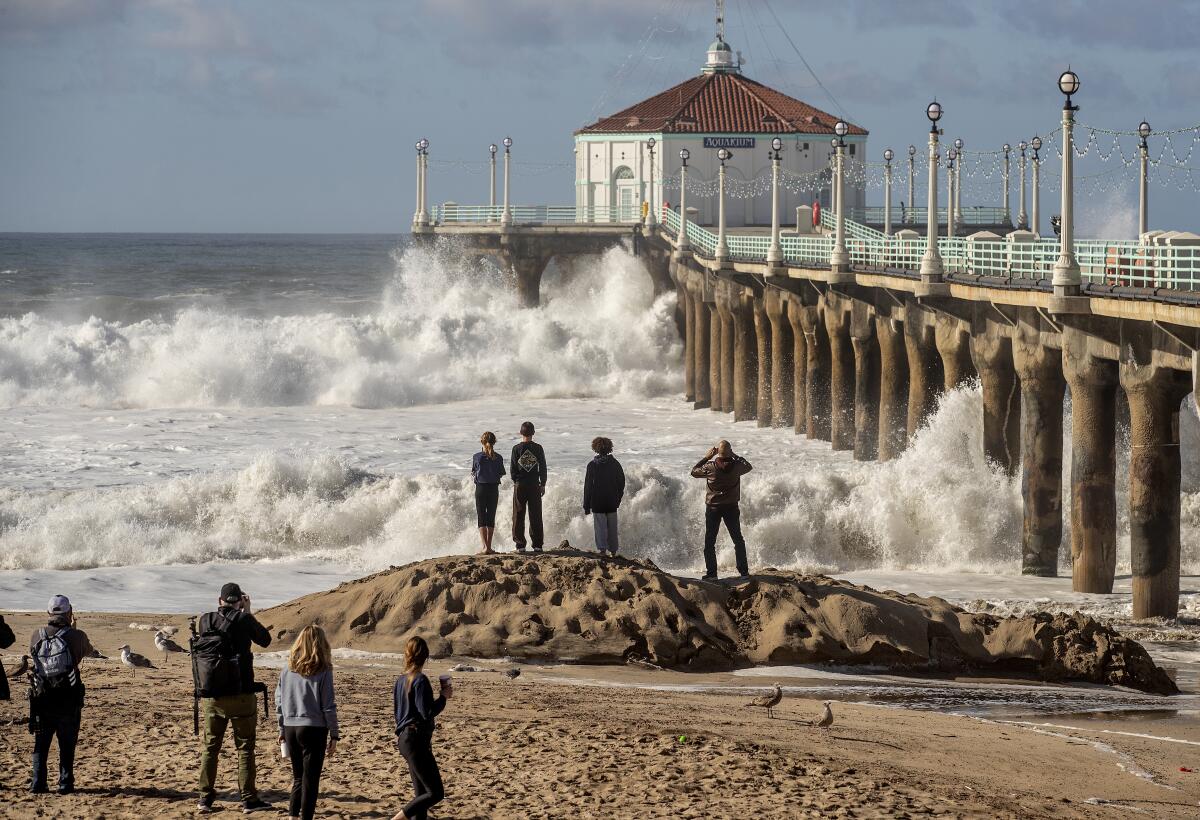 People watch and photograph as a large wave crashes against the Manhattan Beach Pier. 