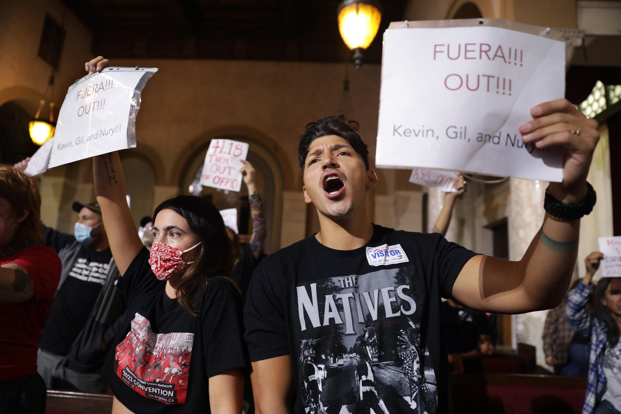 Two protesters hold signs inside council chambers