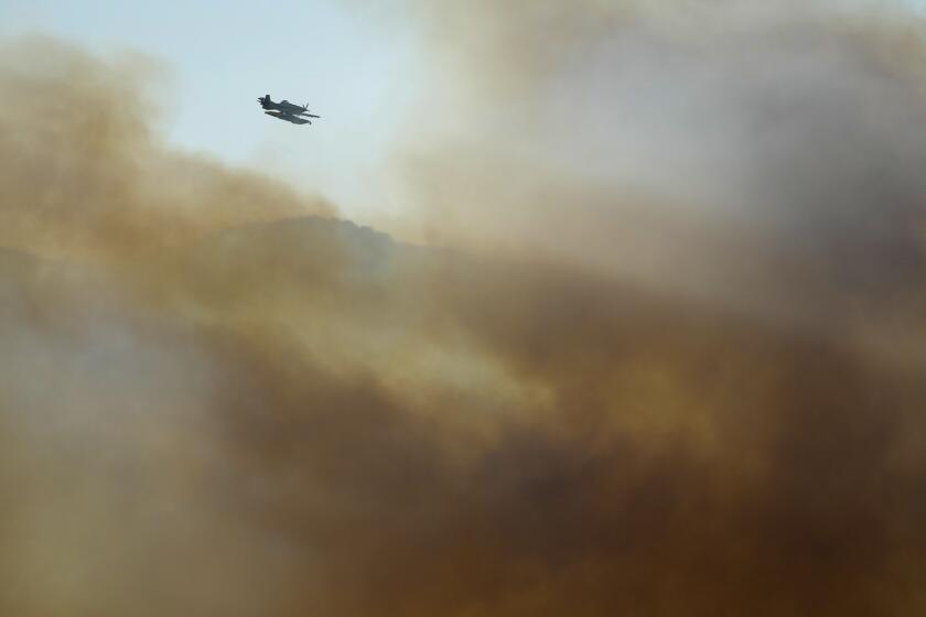 A firefighting airplane flies above clouds of smoke from a wildfire burning near houses in Alcabideche, outside Lisbon, Tuesday, July 25, 2023. Hundreds of firefighters and over a dozen airplanes were fighting a wildfire that spread quickly fanned by strong winds. (AP Photo/Armando Franca)