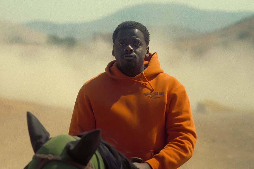 A man in an orange hoodie riding a horse in the desert