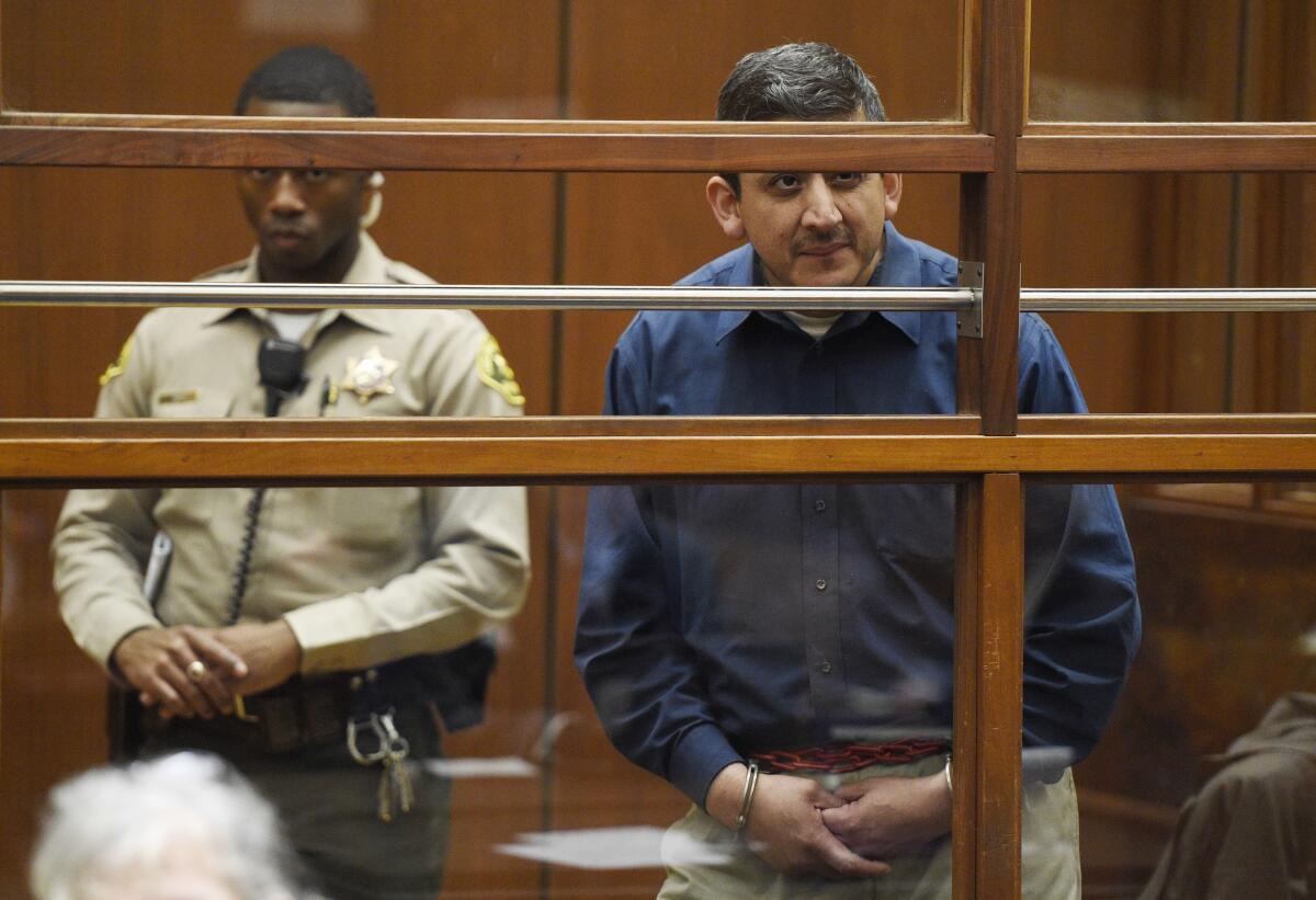 Ramiro Valerio is seen behind glass, wearing handcuffs