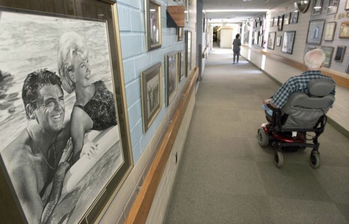 An elderly man in a wheelchair in a nursing home hallway