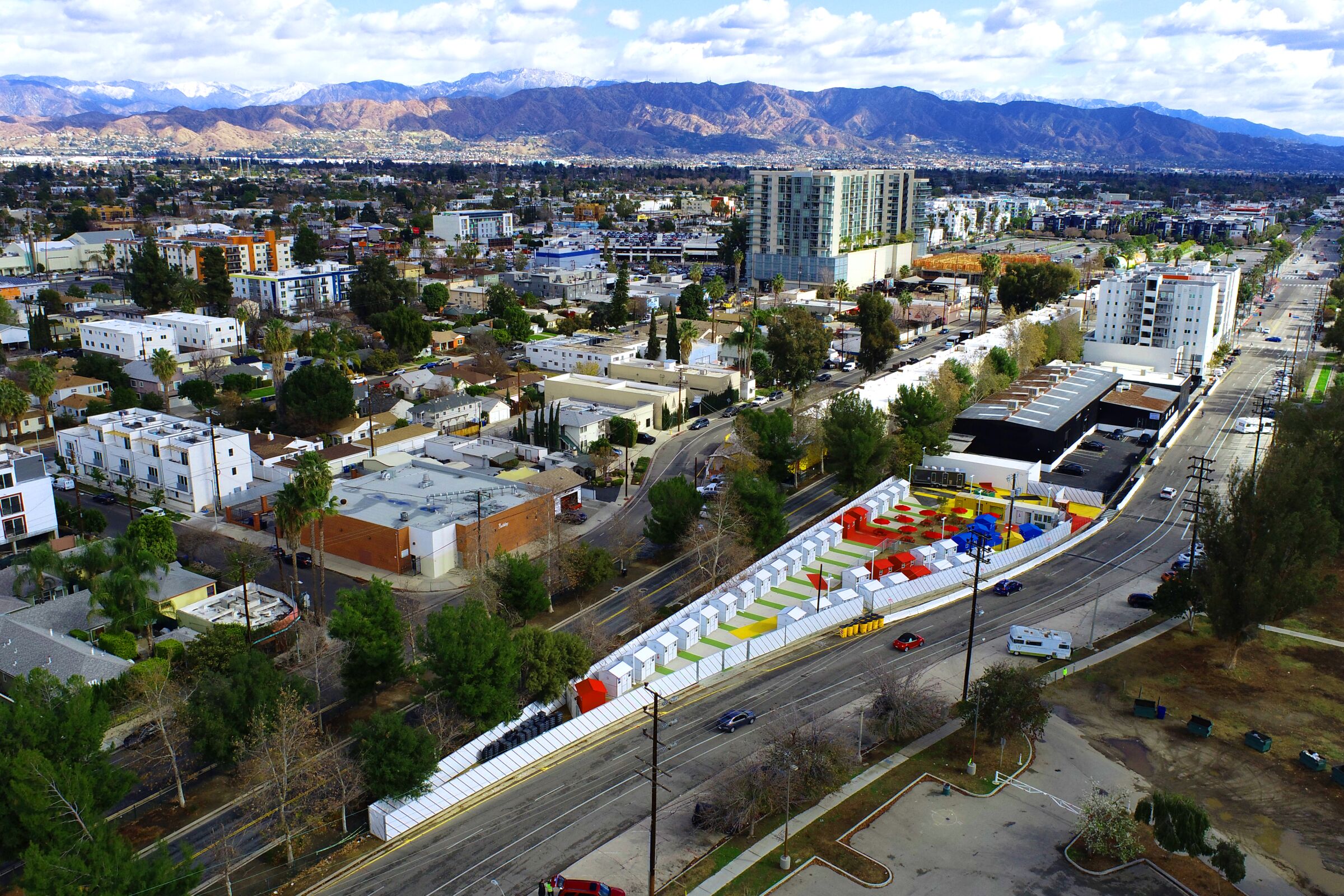 An aerial view shows tiny homes in shades of white, red, blue and yellow tucked into a narrow triangle of land