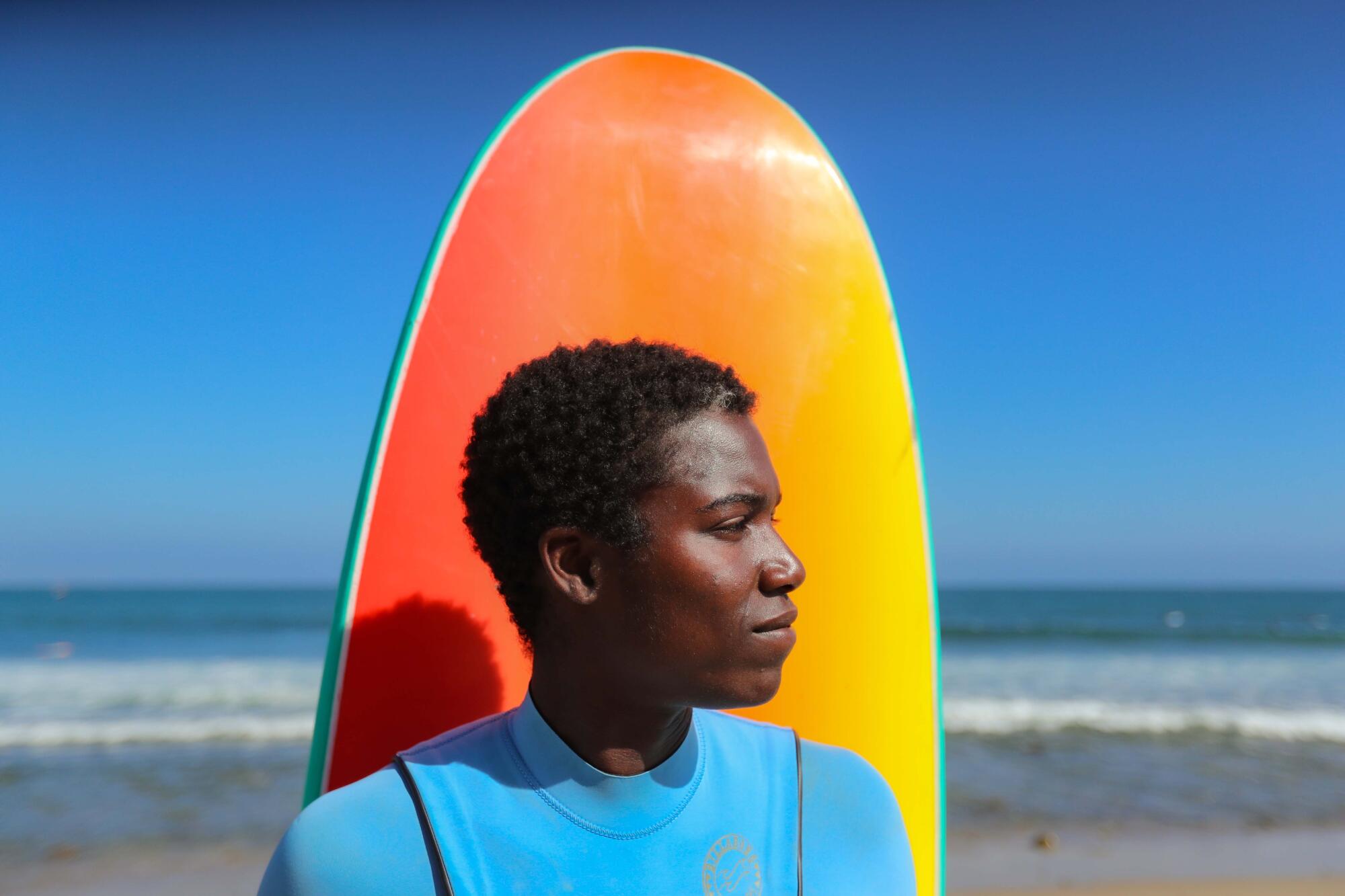 A person poses in front of a surfboard and the ocean.