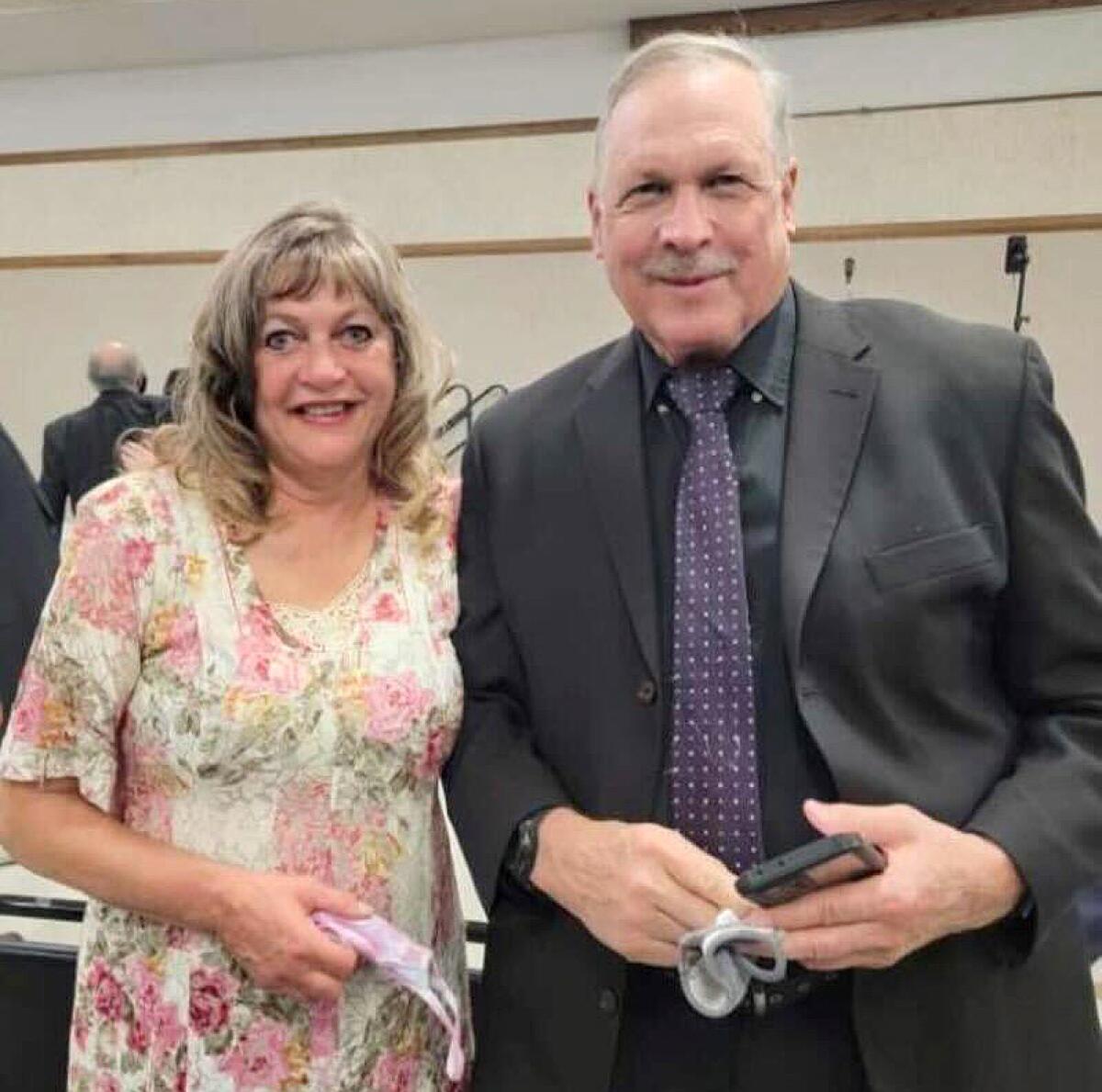 A woman in a flowered dress stands with a man in a dark suit and tie.