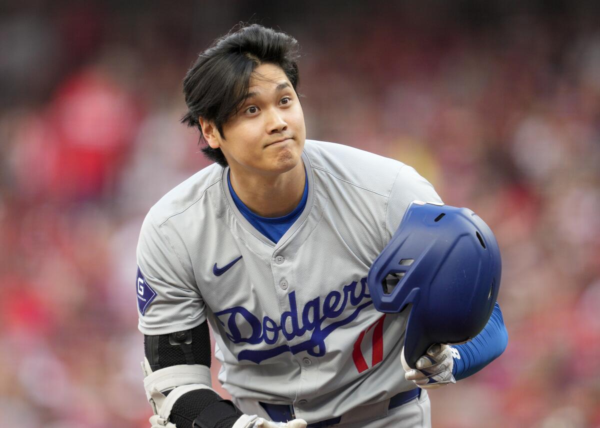 Dodgers star Shohei Ohtani picks up his helmet during an at-bat in the first inning against the Reds on Saturday.