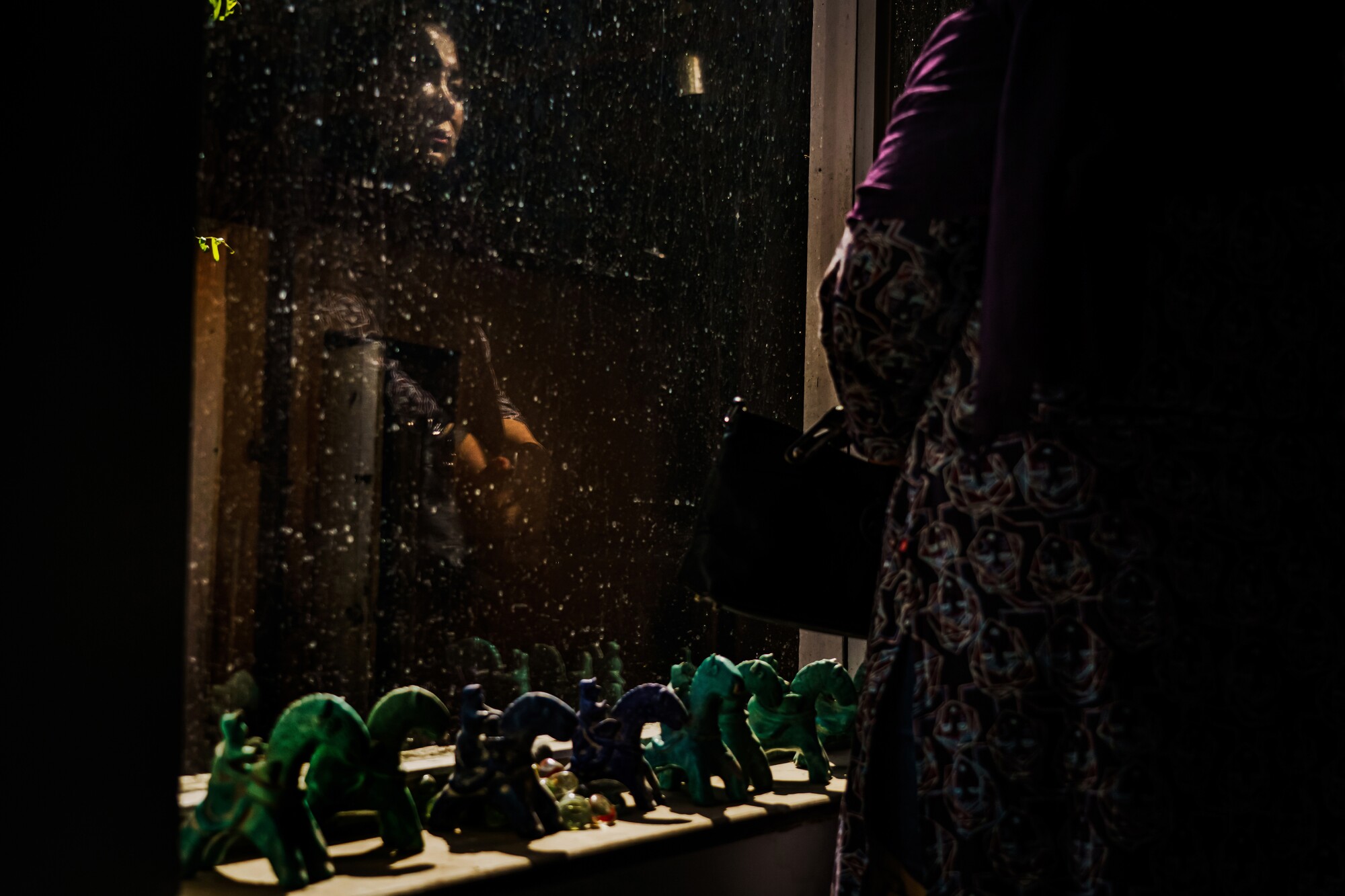 A weeping woman is reflected in a window, green horsemen figurines line the sill.