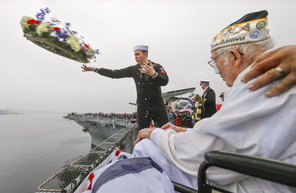 A Navy sailor tosses a wreath into the ocean