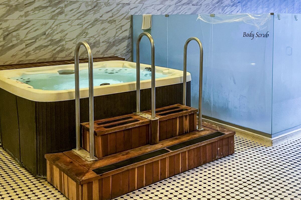 A square Jacuzzi with wooden steps, next to a blue wall with the words Body Scrub on it.