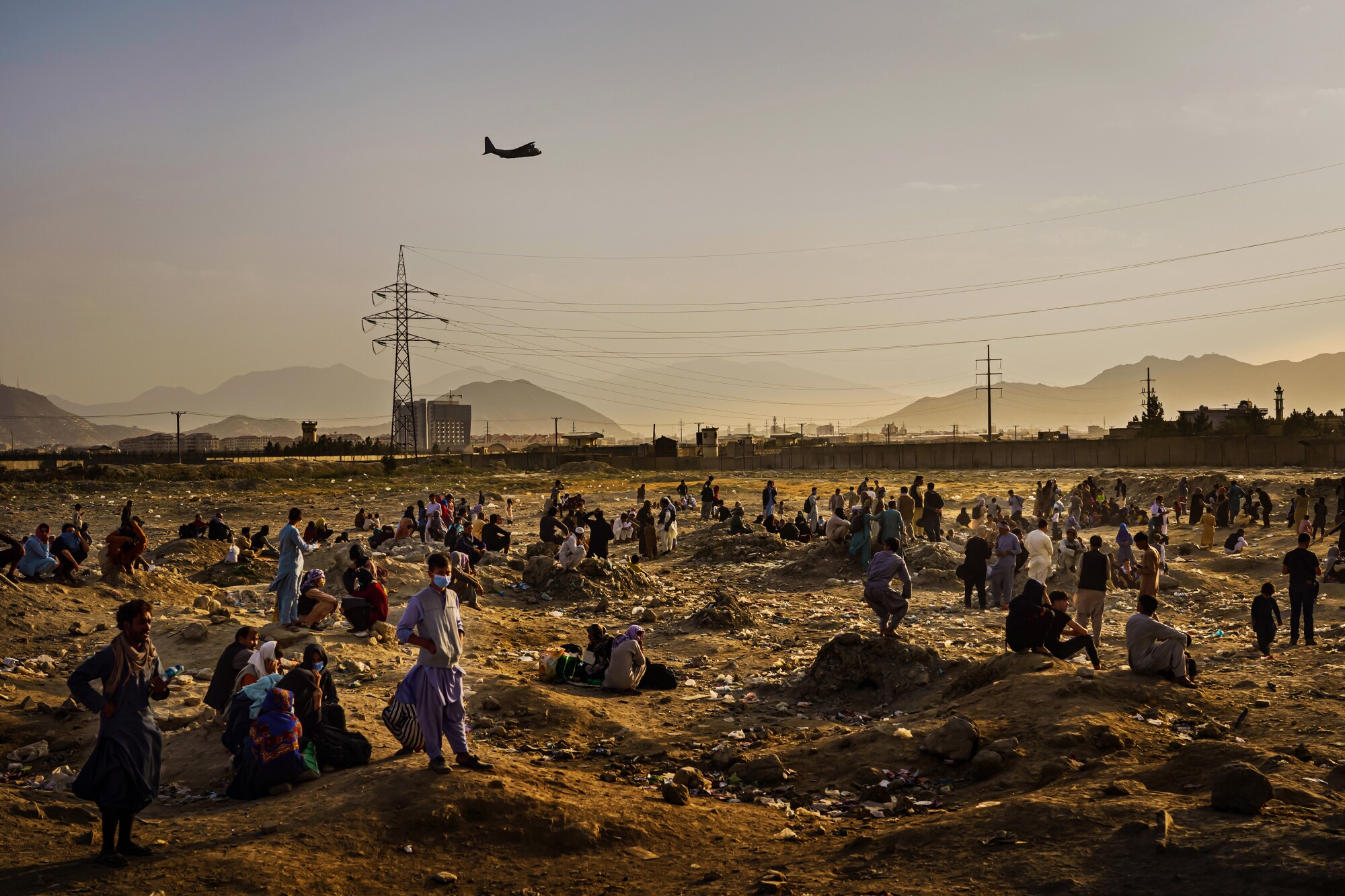 A military transport plane departs as Afghans stand in a field below.