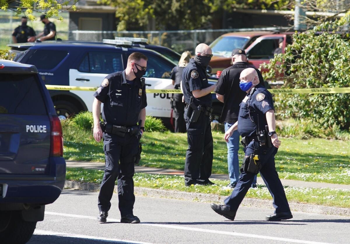 Police walk around road and grass near police vehicles and yellow tape