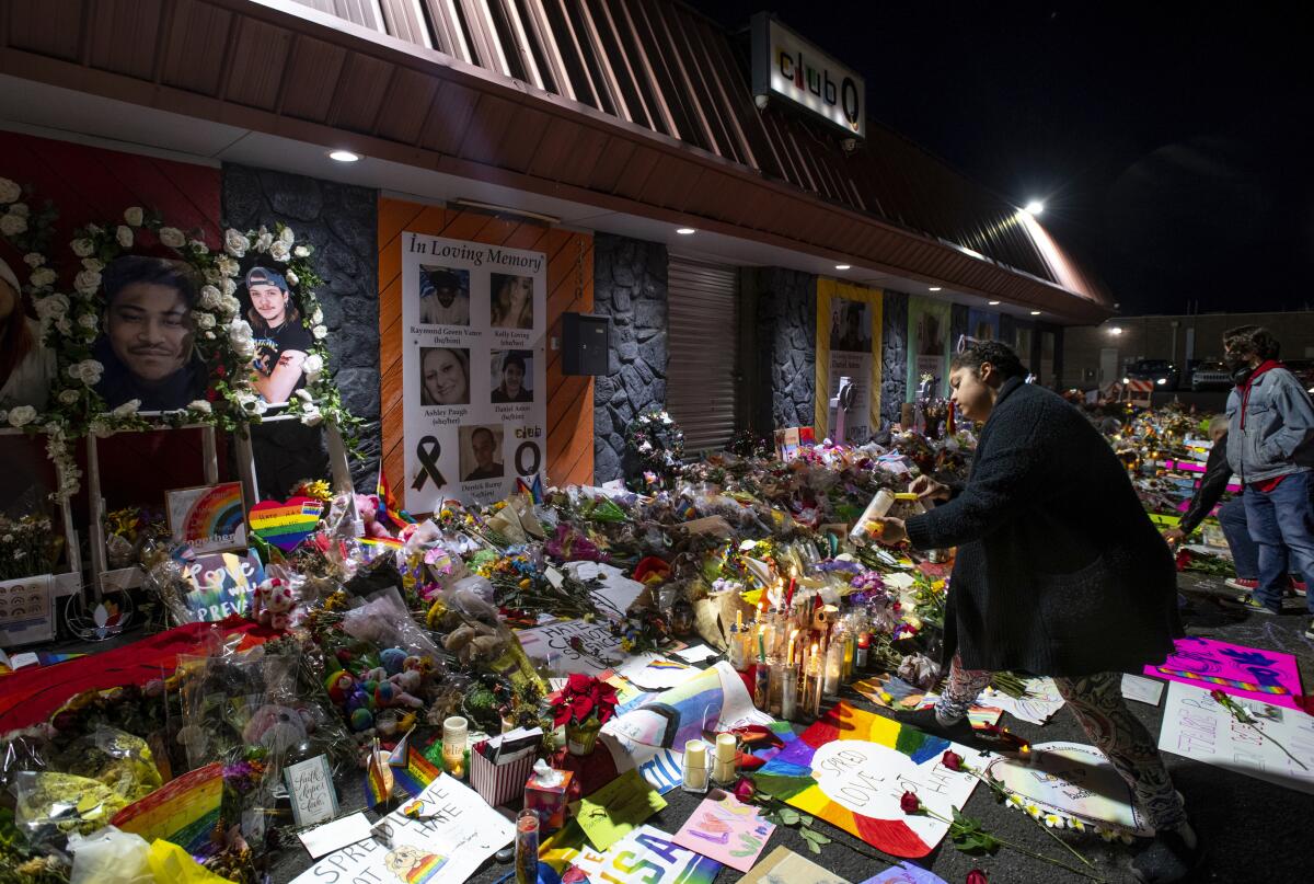 A mourner lights candles at a memorial covered with photos, flowers, cards and posters outside Club Q.