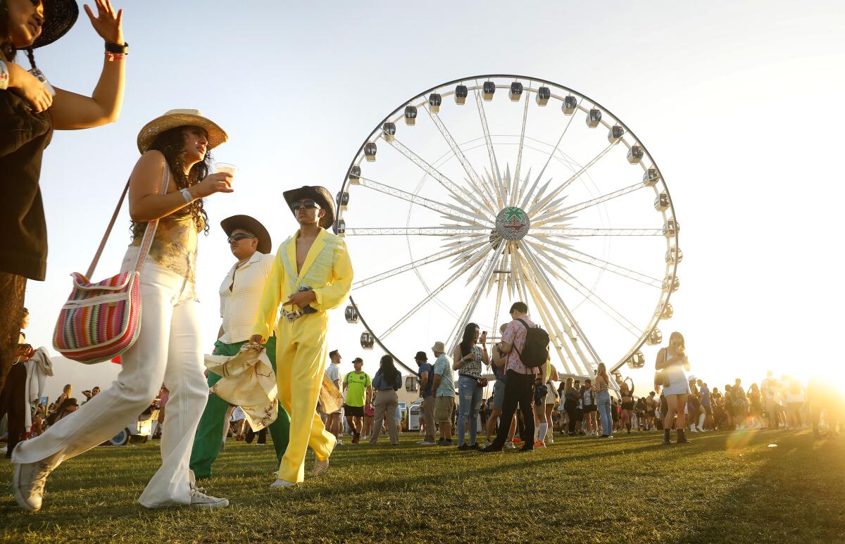 Coachella festival-goers wearing cowboy attire walk on grass in front of a ferris wheel 