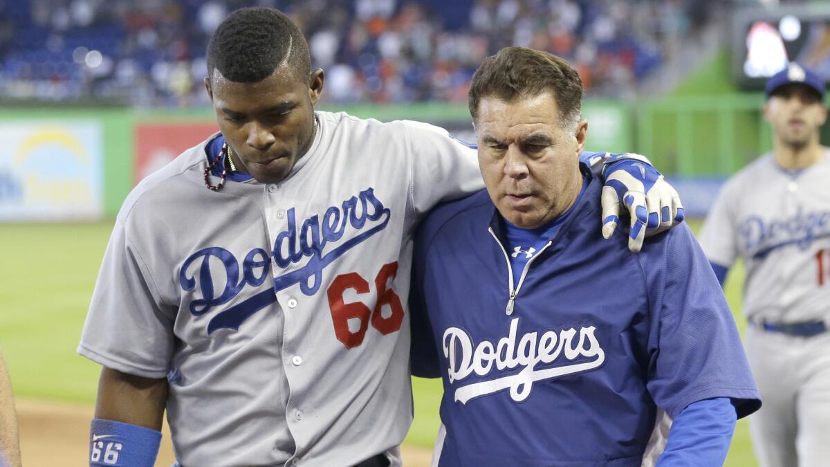 Dodgers right fielder Yasiel Puig, left, is helped off the field by a trainer after colliding with the outfield fence while chasing after a hit during the ninth inning of the team's 5-4 loss to the Miami Marlins on Sunday.