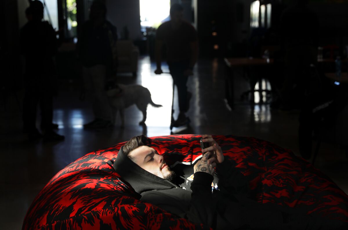 A person in a dark hoodie lies on a red covered sofa at FaZe Clan's headquarters in Los Angeles.