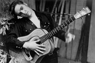 Rock and roll singer Elvis Presley poses for a portrait holding an acoustic guitar in 1956