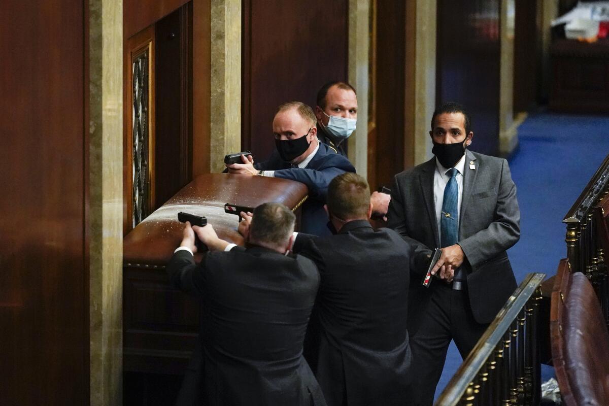 U.S. Capitol Police with guns drawn stand near a barricaded door as protesters try to break into the House Chamber.