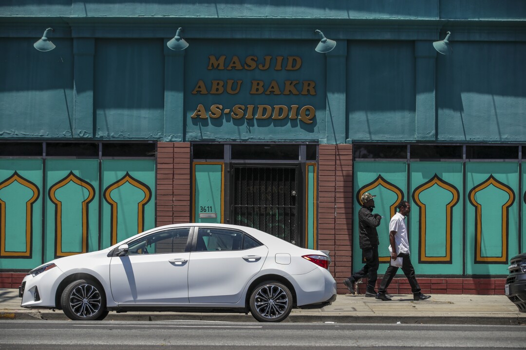 Two men walk past the exterior of a building labeled Masjid Abu Bakr As-Siddiq