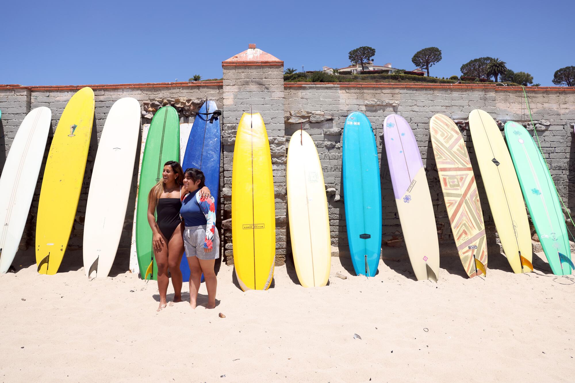 Giselle Carrillo poses for a photo with Genesis Mendoza in front of a row of longboards at First Point in Malibu.