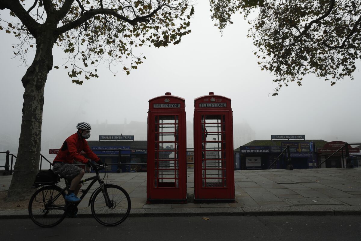 FILE - A cyclist wearing a face mask passes traditional red phone boxes, in London, on Nov. 5, 2020. Thousands of Britain’s iconic red phone boxes will be protected from removal under new rules, the telecoms regulator said Tuesday, Nov. 9, 2021. The public payphone boxes may appear obsolete relics to many in an age of smart mobile phones, but the telecoms regulator, Ofcom, said they can still be a “lifeline” for people in need. The regulator is proposing rules to prevent 5,000 phone boxes in areas with poor mobile coverage from being closed down. (AP Photo/Matt Dunham, File)