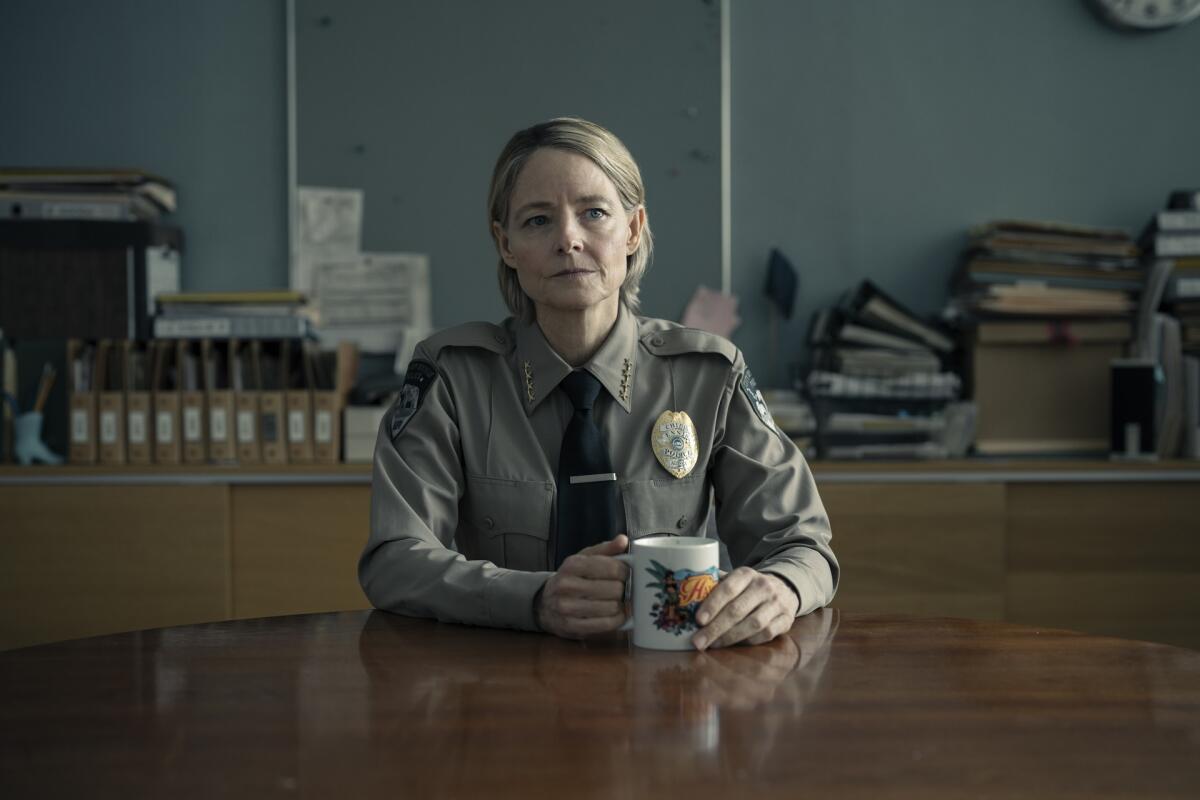 Jodie Foster as a police officer sits at a table with a coffee mug.