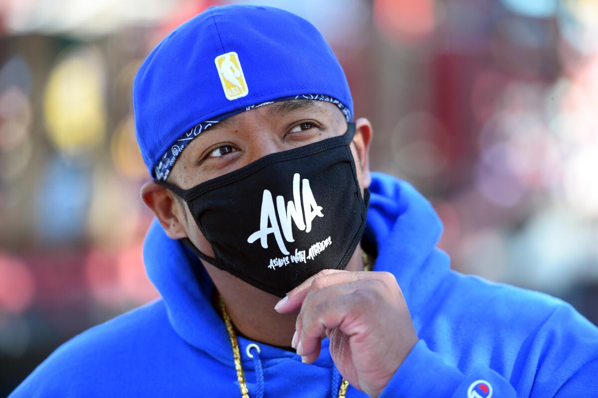 A man in a blue hoodie and backwards cap with a black mask that says AWA: Asians With Attitude