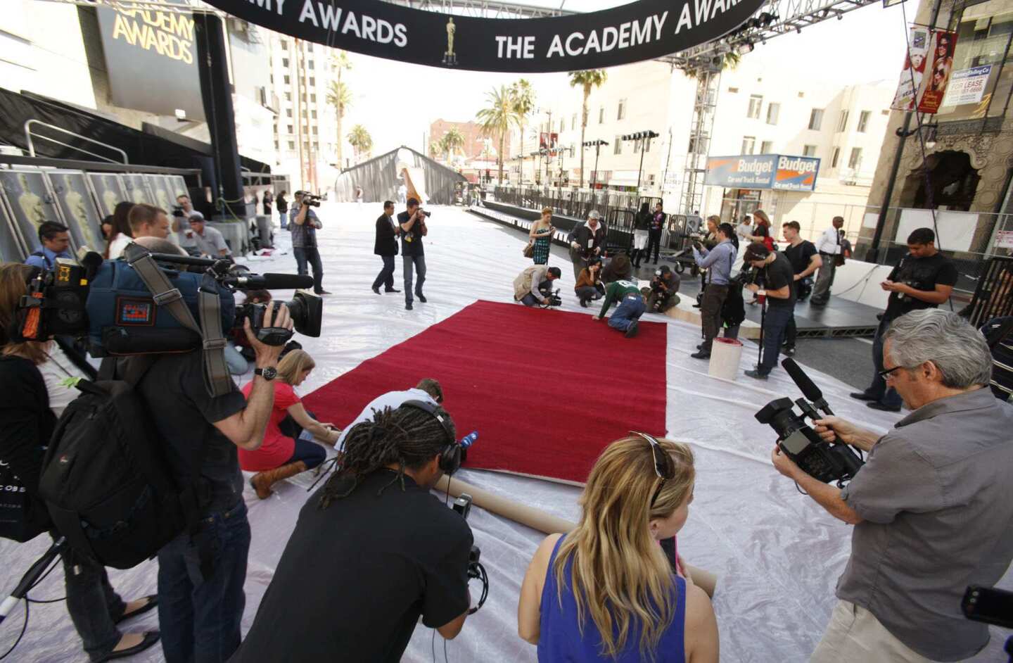 Members of the media crowd around for a shot as workers roll out the red carpet.