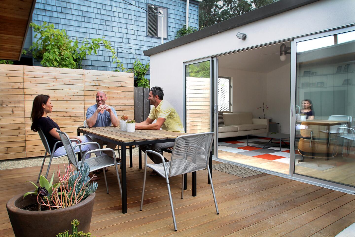 Maria Torres and Joe Borst, center, sit with Robert Sweet at the outdoor dining room just off of the newly expanded living room. Because of their budget, Sweet cut standard dog-eared cedar fence boards and installed them horizontally for more of custom look, and sliding glass doors were used instead of a costly folding NanaWall with the thought that the latter could be added in the future.